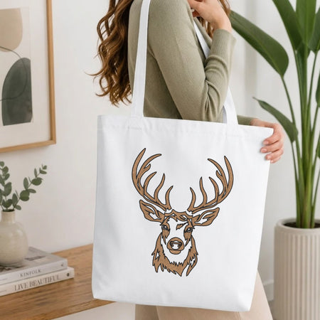  Woman carrying a white natural canvas tote bag featuring an embroidered deer head design in a bright, modern interior setting   