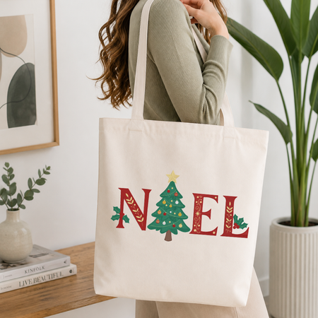 Woman carrying a white natural canvas tote bag featuring a "NOEL" Christmas tree machine embroidery design in a bright, modern interior setting
