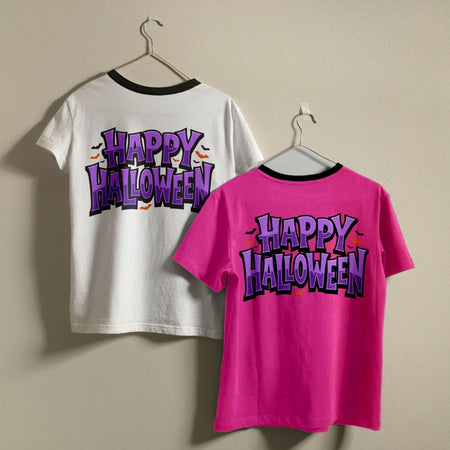 Two t-shirts hanging on a wall—one white and one bright pink—both featuring the purple "Happy Halloween" back print design.