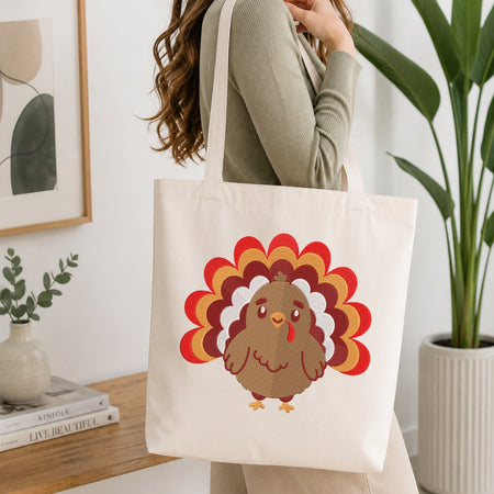 A woman wearing a ribbed sage green long-sleeve top carries a cream canvas tote bag with a cartoon turkey graphic. The turkey has a brown body and a red, orange, and yellow feather pattern.