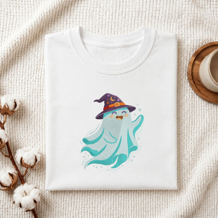 Folded white cotton t-shirt mockup featuring a blue witch ghost machine embroidery design, styled with cotton stems and a wooden cup   