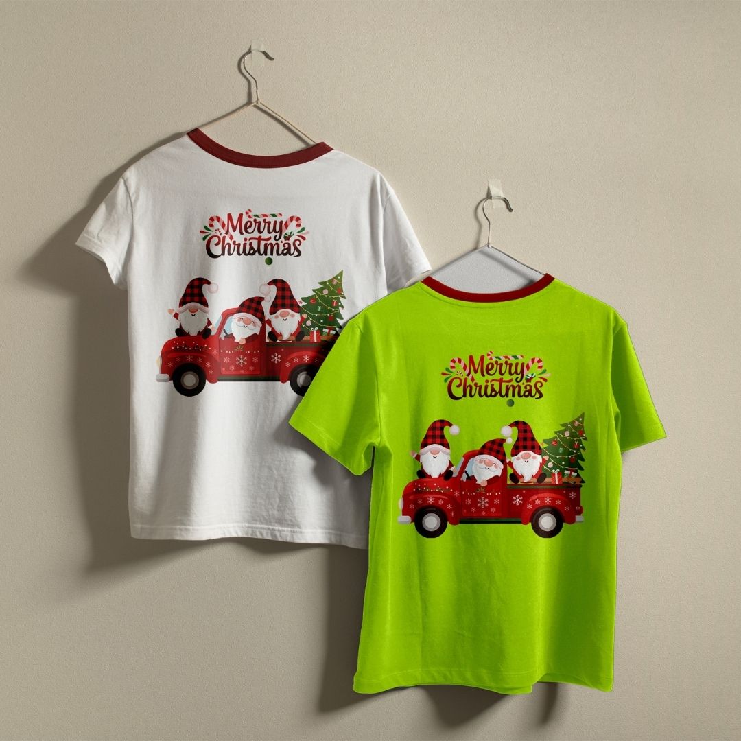 Two Christmas-themed ringer t-shirts displayed on hangers against a plain beige wall. One shirt is white with a red collar and features a back graphic of gnomes in a red truck with 'Merry Christmas' text.