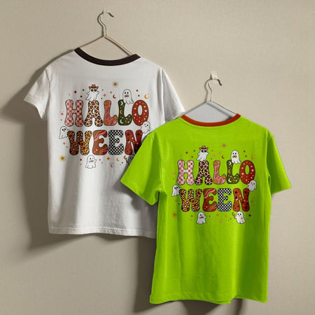 Two children's Halloween-themed short-sleeve t-shirts hanging on hangers against a plain beige wall. The left shirt is white with a dark brown collar and features a colorful 'HALLOWEEN' graphic on the back with a cowboy, ghosts, and spooky details.