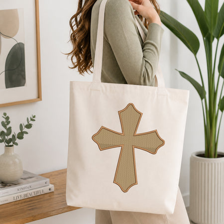 Woman carrying a beige canvas tote bag customized with a brown ornate scalloped cross embroidery design.