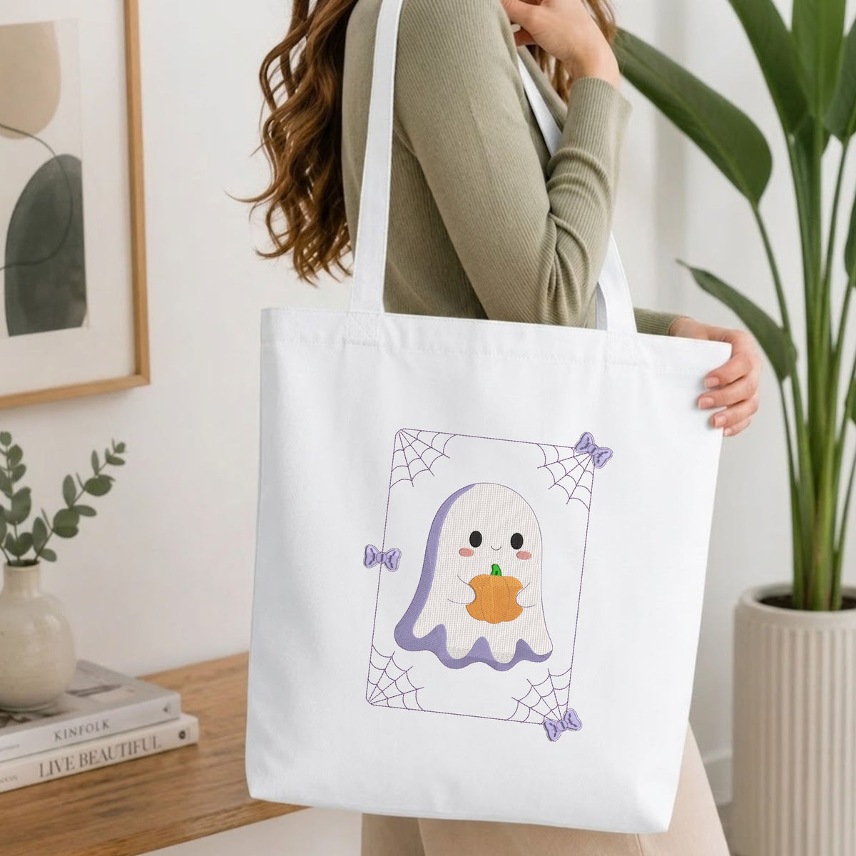 Folded white cotton t-shirt mockup featuring a cute ghost machine embroidery design, styled with cotton stems and a wooden cup