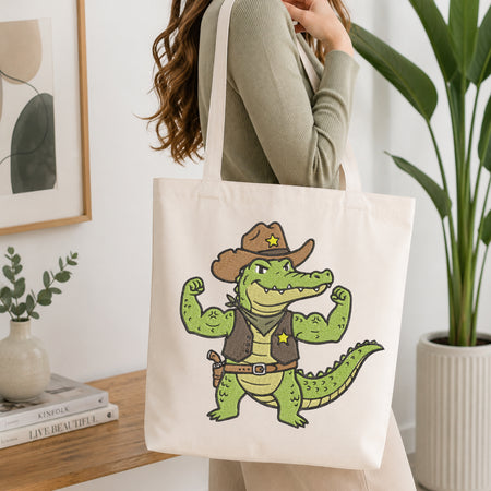 Person holding a white canvas tote bag styled with a cowboy alligator embroidery patch design.