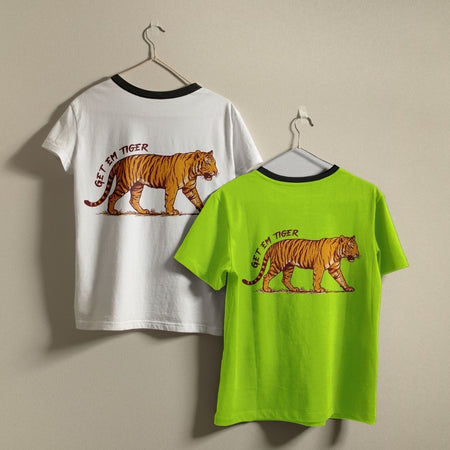 Two ringer t-shirts with black neck trims hanging on metal hangers against a beige wall. The left shirt is white and features a back graphic of an orange tiger with the text 'GET EM TIGER'.