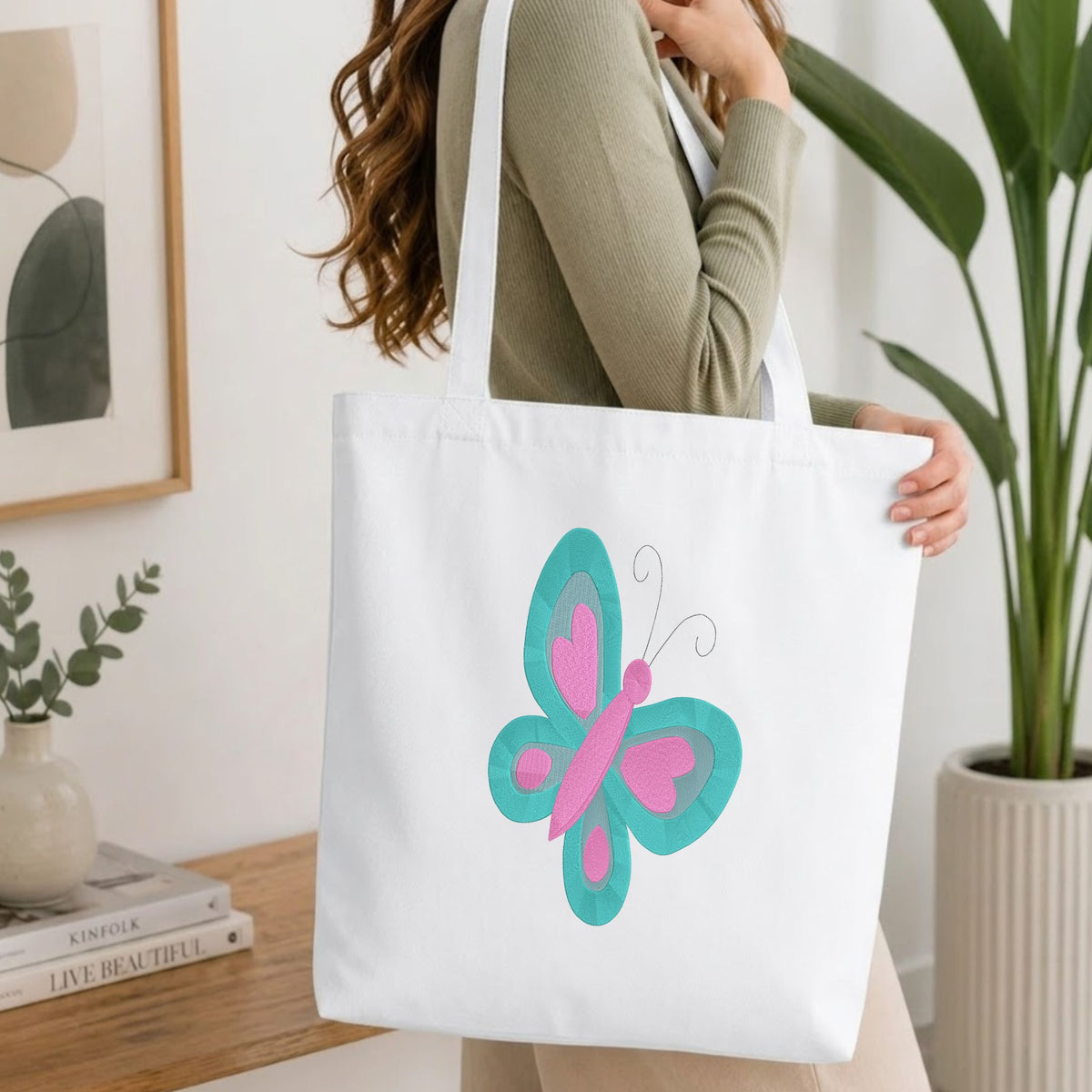 Folded white cotton t-shirt mockup featuring a butterfly machine embroidery design, styled with cotton stems and a wooden cup