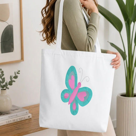 Folded white cotton t-shirt mockup featuring a butterfly machine embroidery design, styled with cotton stems and a wooden cup