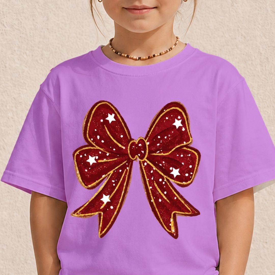 A young girl wearing a light purple short-sleeved t-shirt decorated with a large, deep red bow graphic outlined in gold glitter and dotted with white stars.