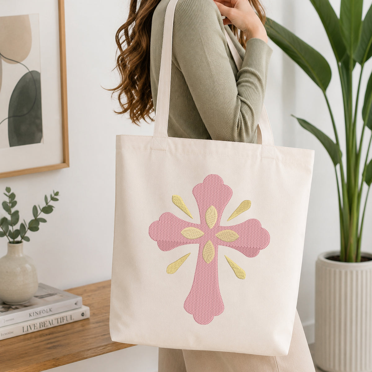 Woman carrying a beige canvas tote bag customized with a pink and gold cross embroidery design.