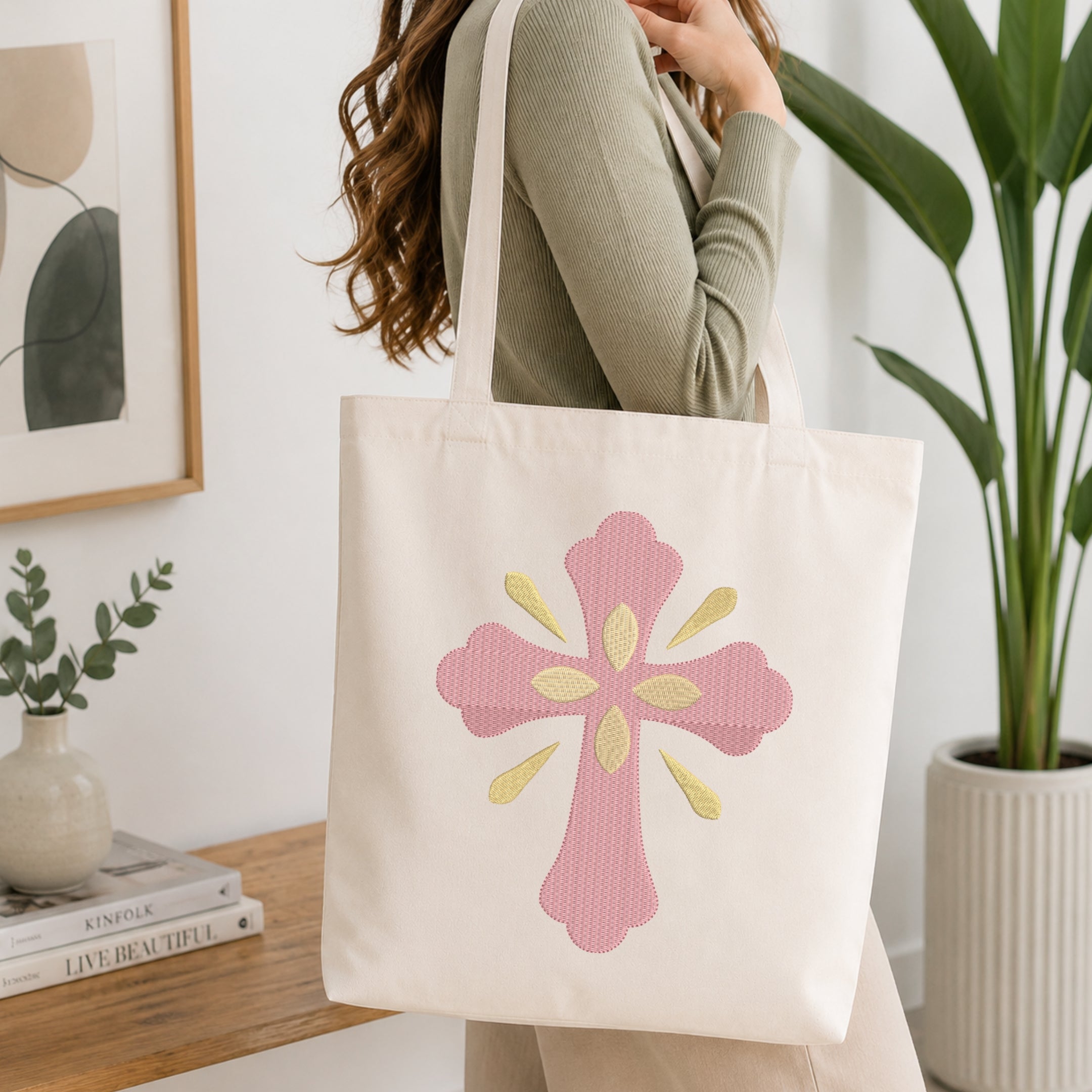 Woman carrying a beige canvas tote bag customized with a pink and gold cross embroidery design.
