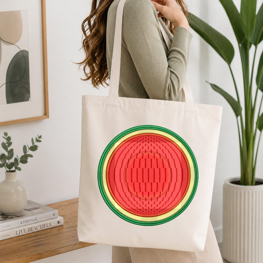 A person wearing a ribbed sage green top carries a cream canvas tote bag featuring a large, colorful watermelon graphic on the front. The setting is a bright, modern room with a wooden table, books, a small vase, and a potted green plant in the background.
