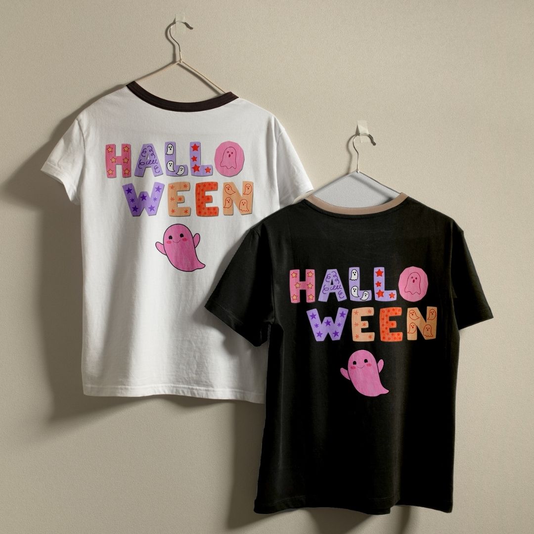 Two Halloween-themed ringer t-shirts, one white and one black, hanging on hangers against a plain beige wall. Both shirts feature a colorful 'HALLOWEEN' graphic with a pink ghost on the back.