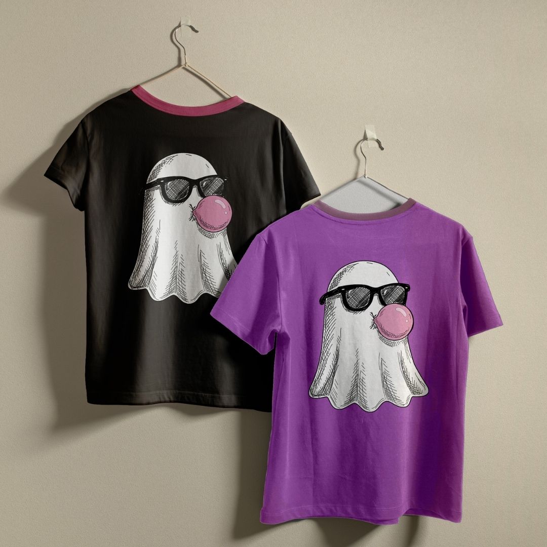 Two short-sleeve graphic T-shirts hanging on hangers against a plain beige wall. The shirt on the left is black with a pink collar trim and features a ghost graphic wearing black sunglasses and blowing a pink bubblegum bubble.