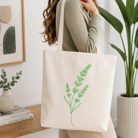 A person carrying a canvas tote bag decorated with the green, line-art embroidered lavender design.