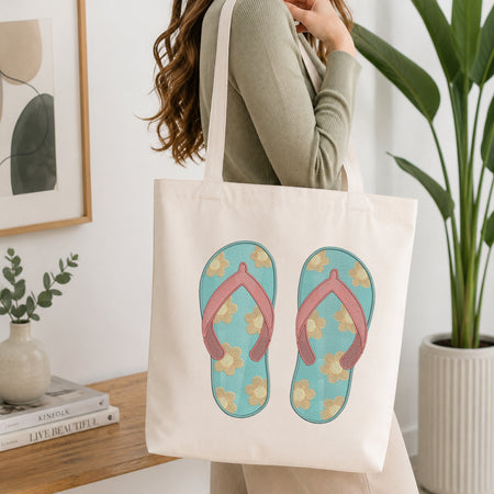 A woman wearing a sage green ribbed long-sleeve top carries a cream canvas tote bag. The bag features a graphic print of a pair of light blue flip-flops with pink straps and yellow floral details.