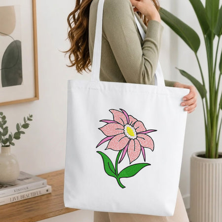 Woman carrying a white natural canvas tote bag featuring an embroidered pink flower design in a bright, modern interior setting