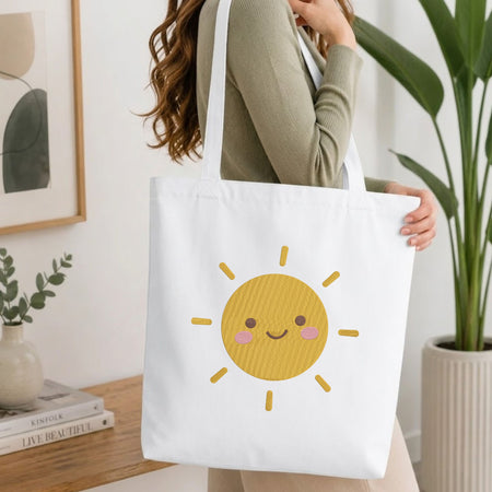 Woman carrying a white natural canvas tote bag featuring a cute smiling sun machine embroidery design in a bright, modern interior setting