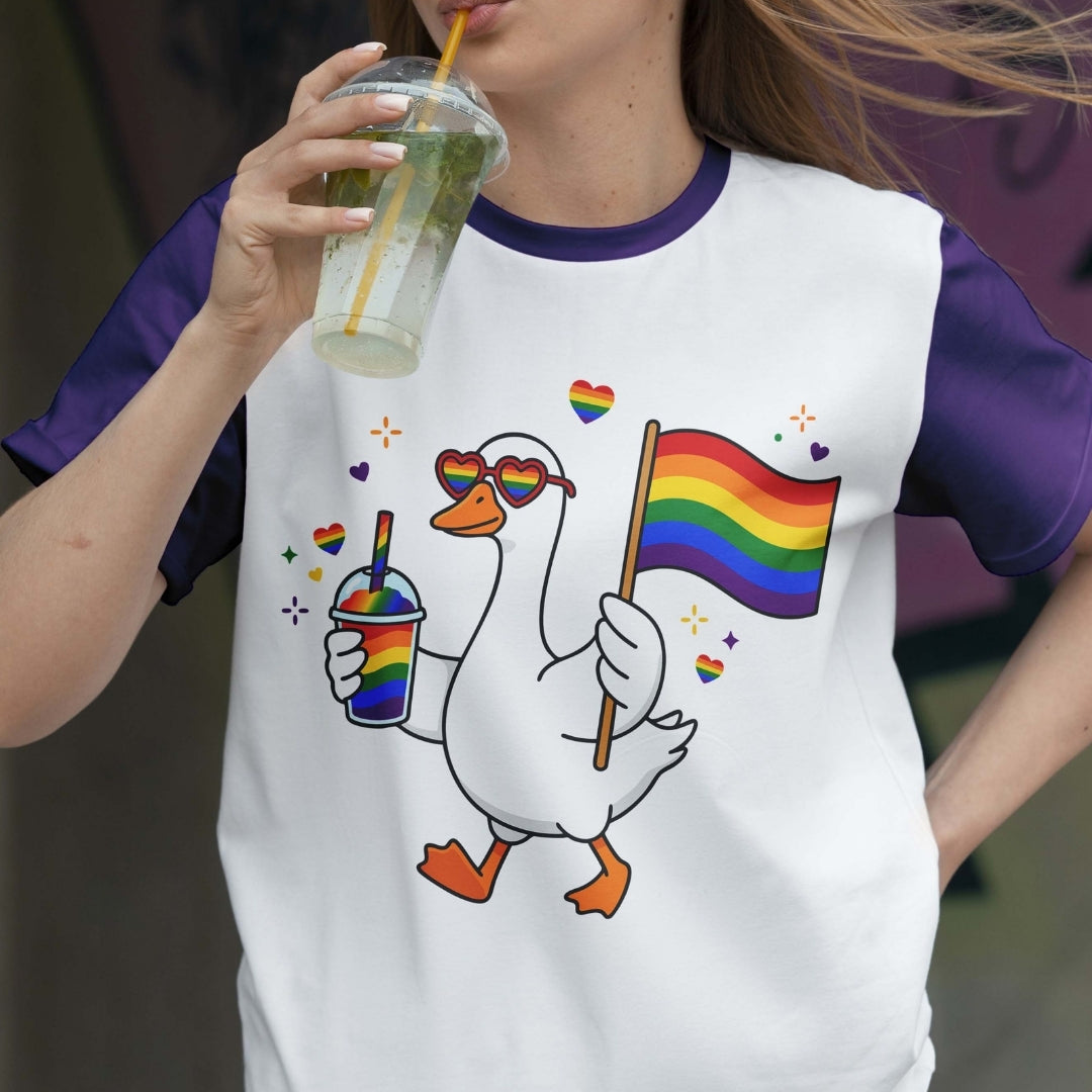 Person wearing a t-shirt with a goose holding a rainbow flag and a drink, drinking from a rainbow-themed cup.