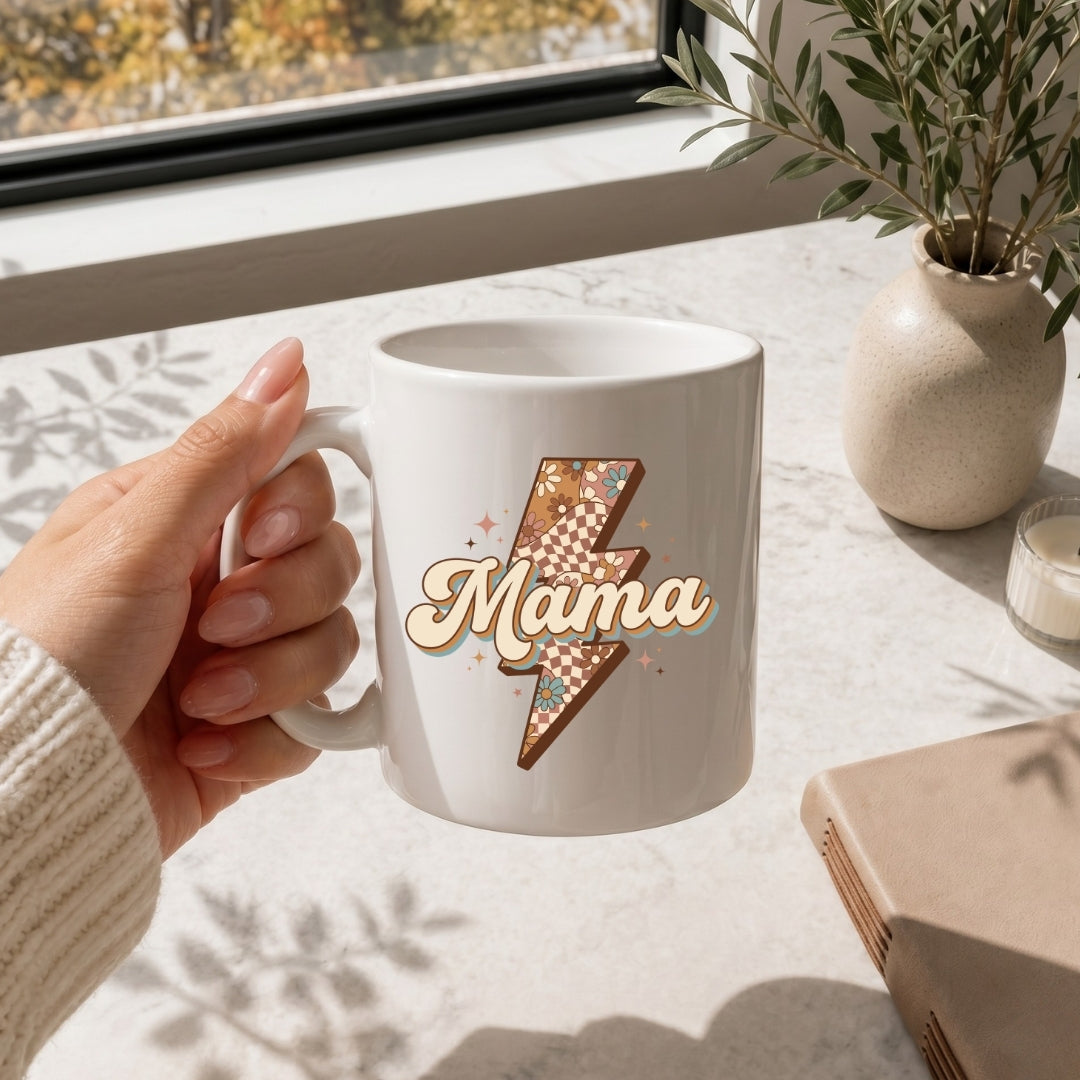 Hand holding a white mug with 'Mama' design on a light surface with a window and plant in the background
