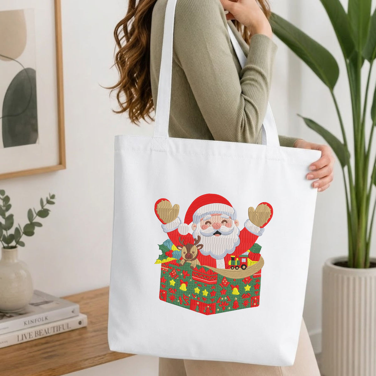Woman carrying a white natural canvas tote bag featuring an embroidered Christmas Santa Claus design in a bright, modern interior setting.