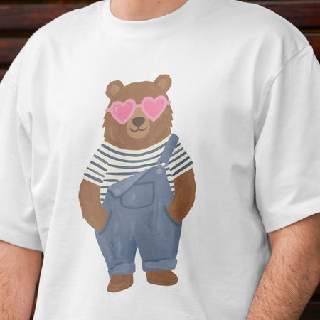 White t-shirt with a bear wearing heart sunglasses and overalls design.