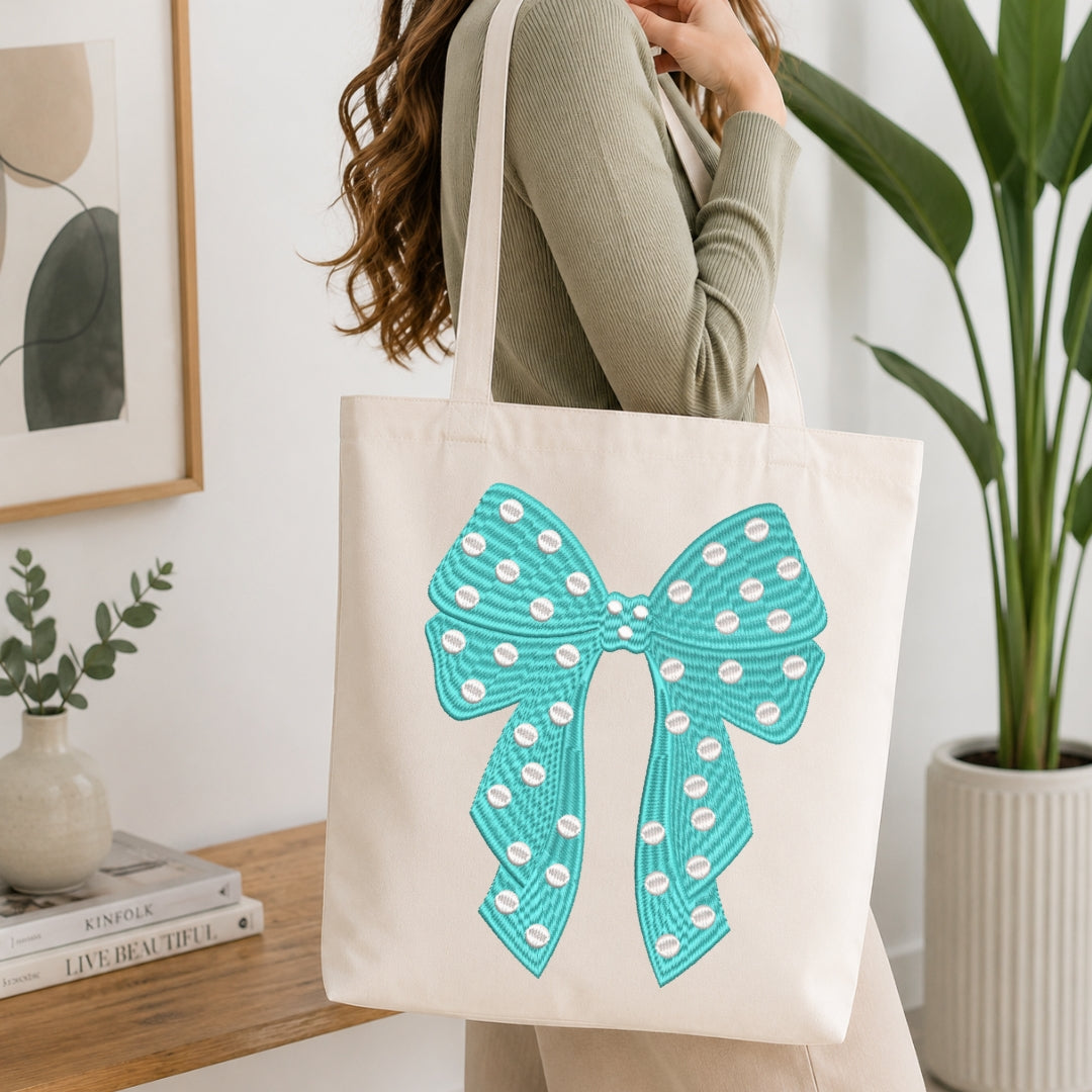 A person carrying a cream-colored tote bag showcasing a teal embroidered polka-dot bow design.