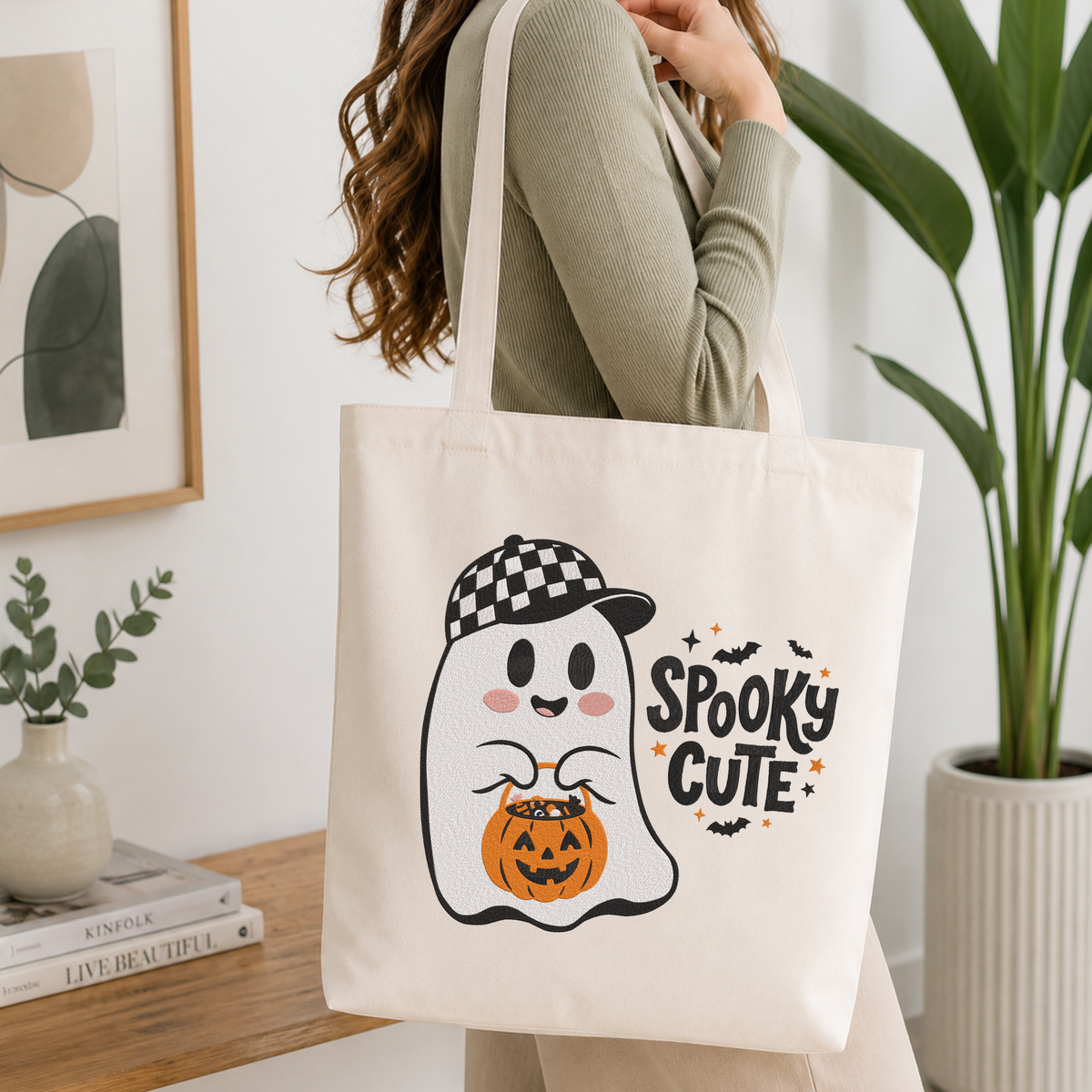  Woman carrying a white natural canvas tote bag featuring a "Spooky Cute" ghost wearing a checkered baseball cap machine embroidery design in a bright, modern interior setting   