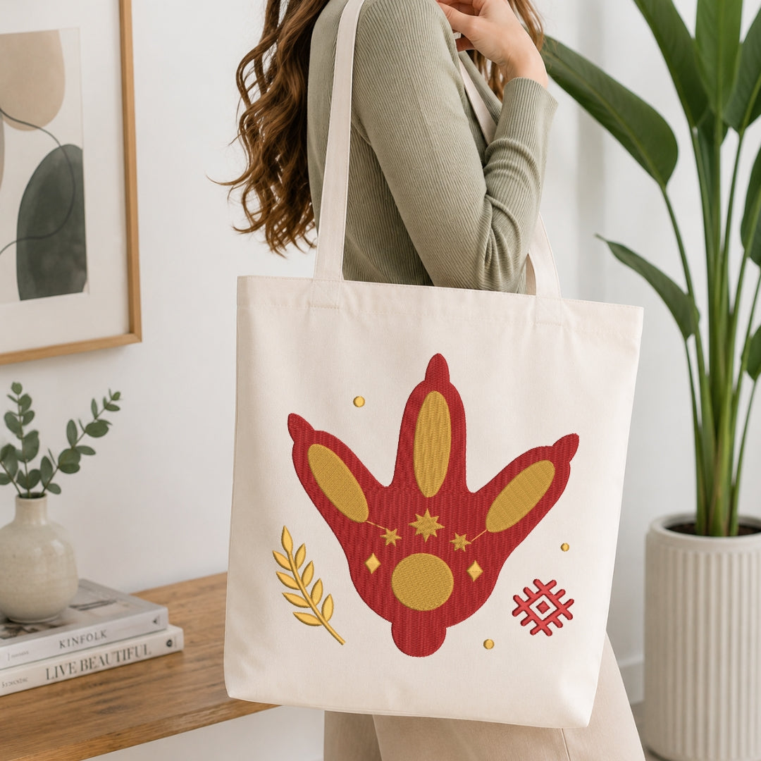 A person is shown from the chest down, carrying a cream-colored canvas tote bag printed with the same mystical footprint embroidery design.