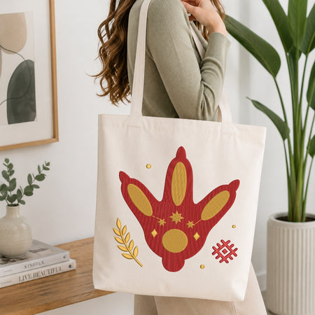 A person is shown from the chest down, carrying a cream-colored canvas tote bag printed with the same mystical footprint embroidery design.