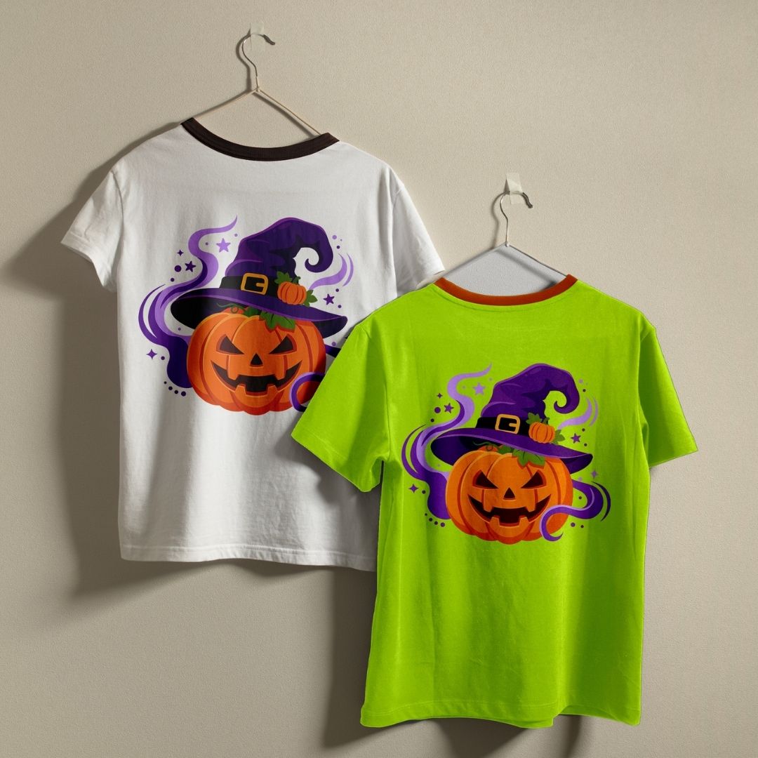 Two children's Halloween-themed t-shirts displayed on hangers against a plain beige wall. One shirt is white with a black collar trim, and the other is neon lime green with a red collar trim.