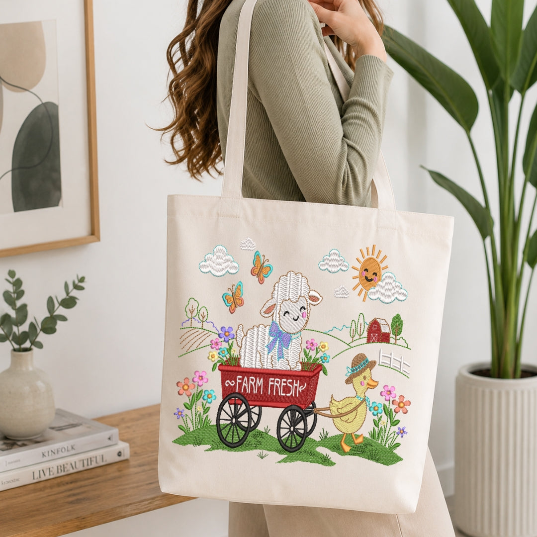 A woman carries a cream canvas tote bag with a colorful cartoon farm illustration featuring a white lamb in a red wagon, a yellow duck, flowers, butterflies, clouds, and a smiling sun. The scene is set in a bright, modern room with a wooden table, books, a framed print, and a potted plant.