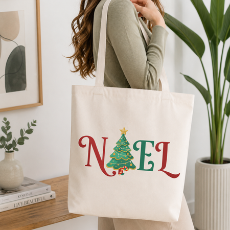 Woman carrying a white natural canvas tote bag featuring a "NOEL" Christmas tree machine embroidery design in a bright, modern interior setting