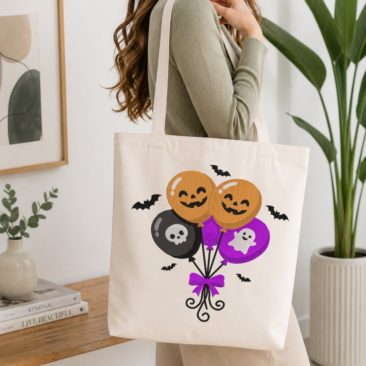 Woman carrying a canvas tote bag displaying a machine embroidery design of cute Halloween balloons with pumpkins, a skull, and a ghost.