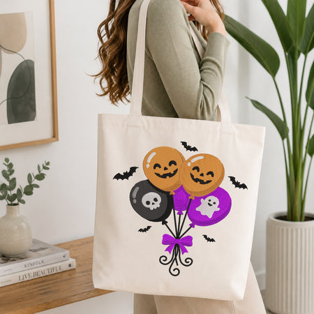 Woman carrying a canvas tote bag displaying a machine embroidery design of cute Halloween balloons with pumpkins, a skull, and a ghost.