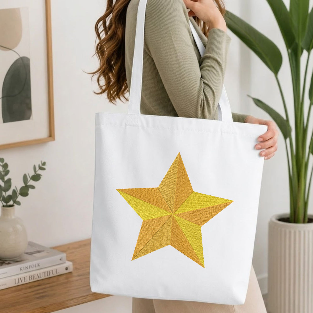 Woman carrying a white natural canvas tote bag featuring an embroidered segmented golden star design in a bright, modern interior setting