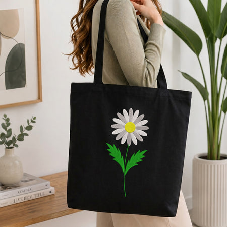 Woman carrying a black canvas tote bag styled with a white daisy flower embroidery pattern.