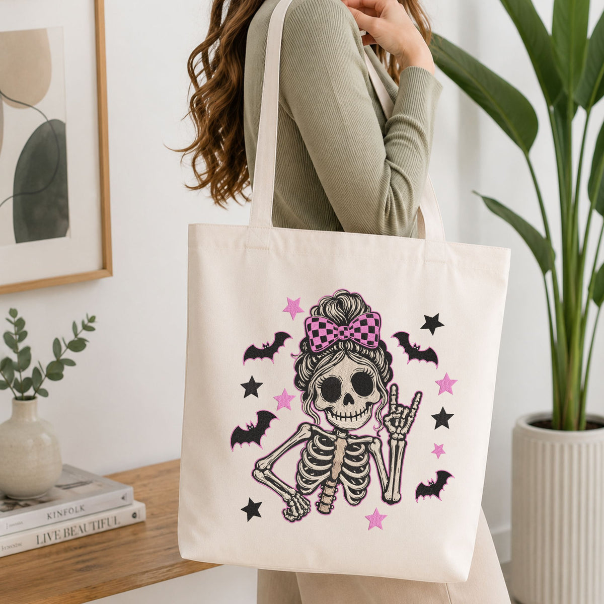 Woman carrying a white natural canvas tote bag featuring a cute skeleton messy bun machine embroidery design in a bright, modern interior setting