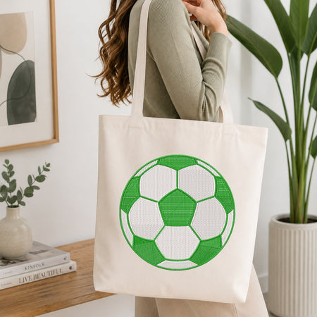 Person holding a tote bag with a green and white soccer ball design in a home setting.