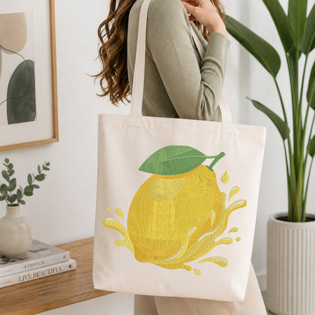 A person carrying a cream-colored canvas tote bag decorated with the embroidered lemon design.