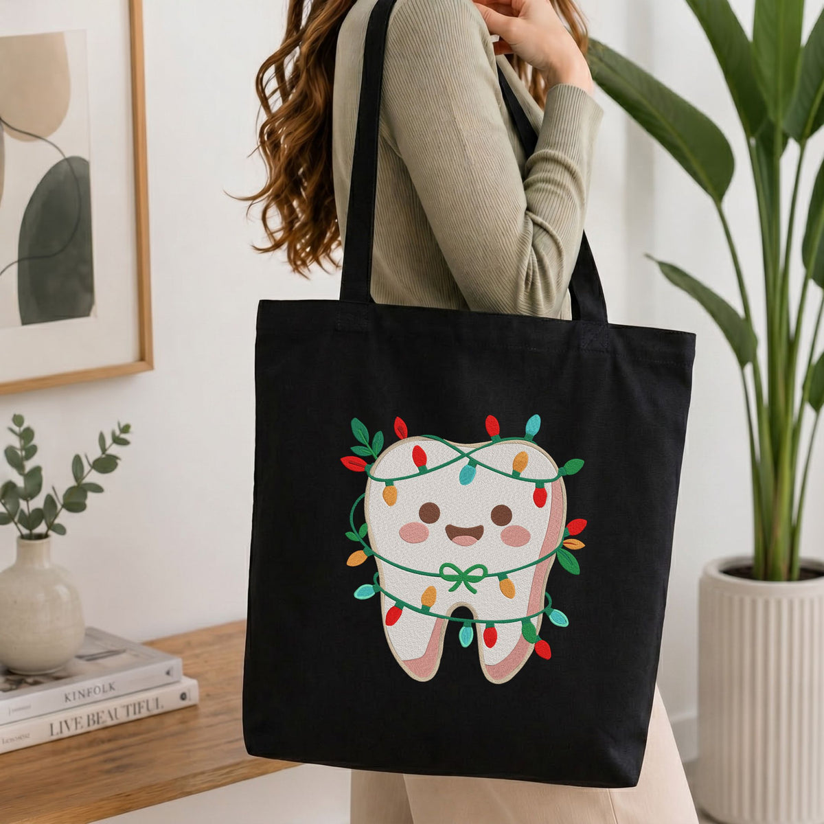 Folded white cotton t-shirt mockup featuring a cute smiling tooth wrapped in Christmas lights machine embroidery design, styled with cotton stems and a wooden cup