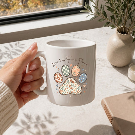 Person holding a mug with paw prints and text on a light surface with a plant in the background