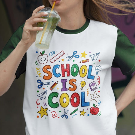 Person wearing a white t-shirt with colorful 'SCHOOL IS COOL' design, holding a drink.