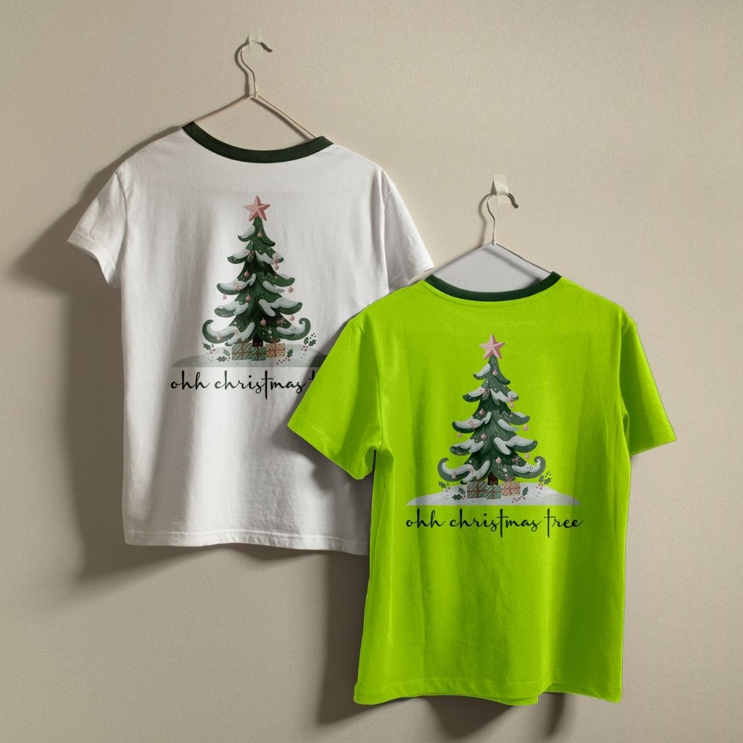 Two t-shirts hanging on a wall—one white and one lime green—both displaying the "ohh christmas tree" holiday graphic print.