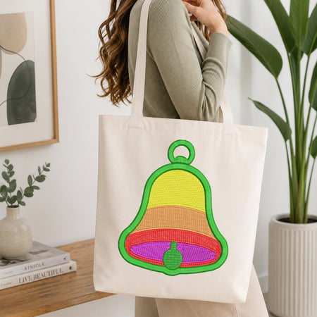 Person holding a tote bag with a colorful bell design in a home setting.