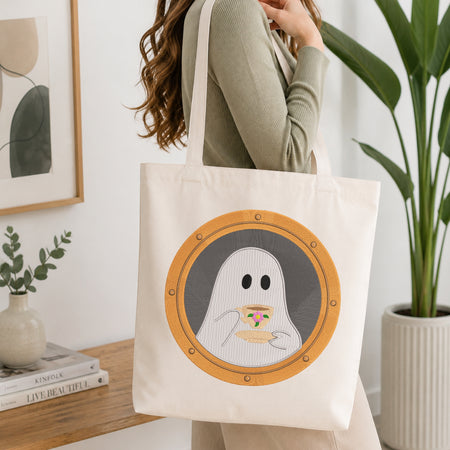 A woman wearing a sage green ribbed long-sleeve top carries a cream canvas tote bag with a graphic of a ghost peeking over a plate of pizza inside a porthole-style circle.