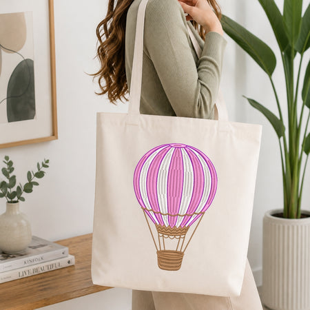 A person is shown carrying a canvas tote bag decorated with the hot air balloon embroidery design.