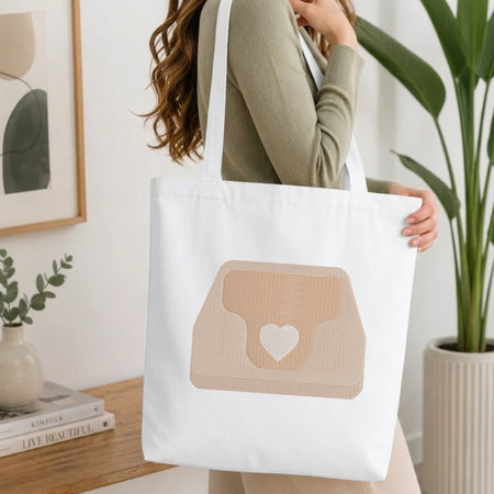 A person holding a natural canvas tote bag printed with an embroidered heart purse design, set against a bright interior room background with green plants.