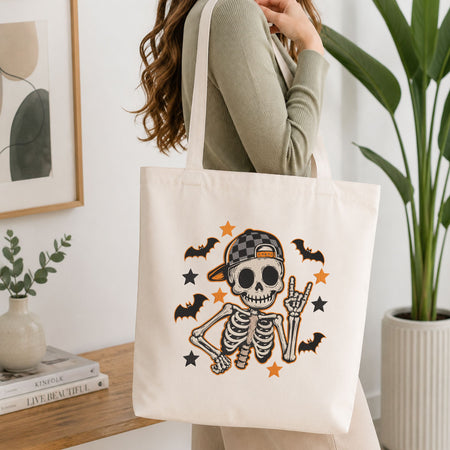 Woman carrying a white natural canvas tote bag featuring a cute skeleton machine embroidery design in a bright, modern interior setting